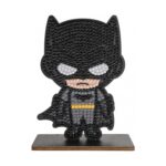 Диамантен гоблен Батман, Craft Buddy: черна фигурка с маска с уши, бели очи и жълт колан, покрита с лъскави кристалчета и изправена на дървена поставка.