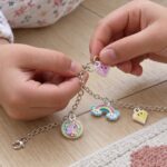 Детски пръсти закачат висулка сърце на верижката на гривната до висулки дъга и еднорог.