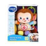 Музикална маймунка за бебе, VTech: кафява маймунка с усмивка, сърце с нота на гърдите и шарени крачета в кутия с надпис „Swing & Sing Monkey“ и логото „vtech Baby“.