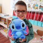Момче с очила държи Стич. Синя плюшена играчка с уши надолу.