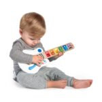 Бебе седи и докосва клавишите на бялата китара Hape Baby Einstein