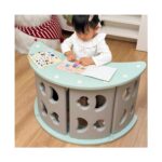 Момиченце разглежда стикери на зеления модул Feelkids, поставен като масичка