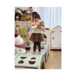 Момиченце стои с плюшена играчка върху зелената катерушка Feelkids в детска стая