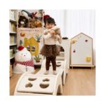 Момиченце стои изправено върху бялата катерушка Feelkids с плюшена играчка в ръце