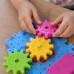 Детски ръце закачат розово зъбчато колело на плоча от 3D конструктор механизми