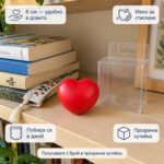 Червено антистрес сърце на рафт до прозрачна кутийка и книги, с надписи за 6 см, меко стискане и побиране в джоб; продава се 1 брой в прозрачна кутийка.