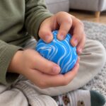 Детски ръце стискат синьо-бялата антистрес топка и пръстите потъват в нея.