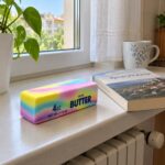 Дъгово скуиши блокче масло на перваза над радиатора, до книга и чаша на сини цветя.