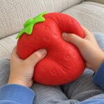 Детски ръце стискат голямата скуиши ягода и тя се сплесква под пръстите.