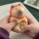Детски ръце стискат скуиши капибарата с оранжева кърпа и резен диня.