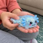 Детски ръце леко притискат синия скуиши аксолотъл с усмихнато личице.