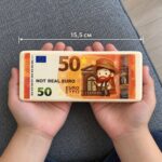 Оранжева скуиши евро банкнота с номинал 50 в две детски длани, с линия за дължина 15,5 см.