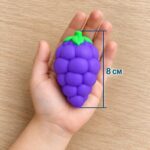Лилавото скуиши грозде в отворена детска длан над дървена маса, с линия за височина 8 см.