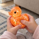 Скуиши пате Jelly Sugar, 7 см: дете стиска прозрачно оранжево скуиши пате пълни с брокат и с черни очички.