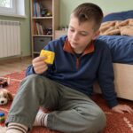 Момче седи на пода, облегнато на леглото, и държи скуиши сиренето между пръстите си.