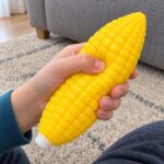 Детски ръце стискат жълтата скуиши царевица и пръстите потъват в релефните зърна.