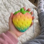 Розово-жълто-синя скуиши ягода в отворена детска длан, с вертикална линия за височина 10 см.