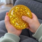 Детски палец натиска средата на златната скуиши монета с брокат.