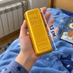 Скуиши златно кюлче в детска длан над синя завивка, с линия за дължина 13 см.