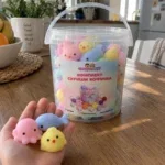 Детска длан държи три мини скуиши, зад нея е кофичката със скуиши