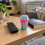 Чаша трицветен Super Slime с топчета на холна маса до дистанционно и книга.